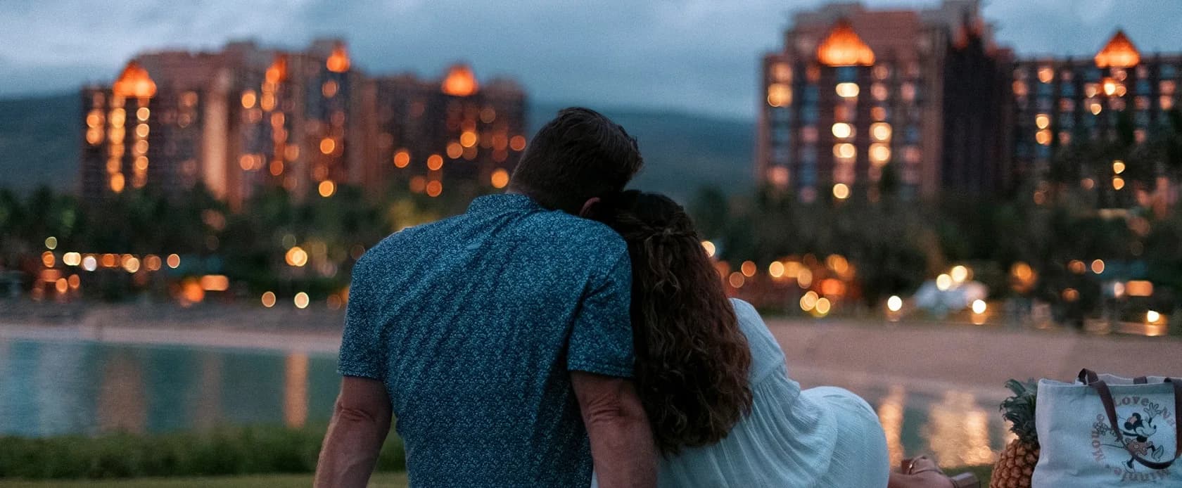 A couple overlooking the lagoon and Aulani Resort at dusk